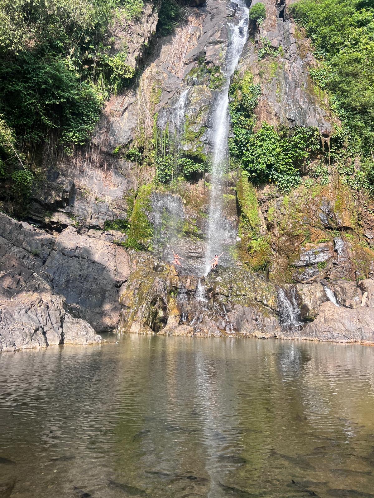 Een waterval die uitmondt in een natuurlijk meertje omringd door steile, bemoste rotsen.