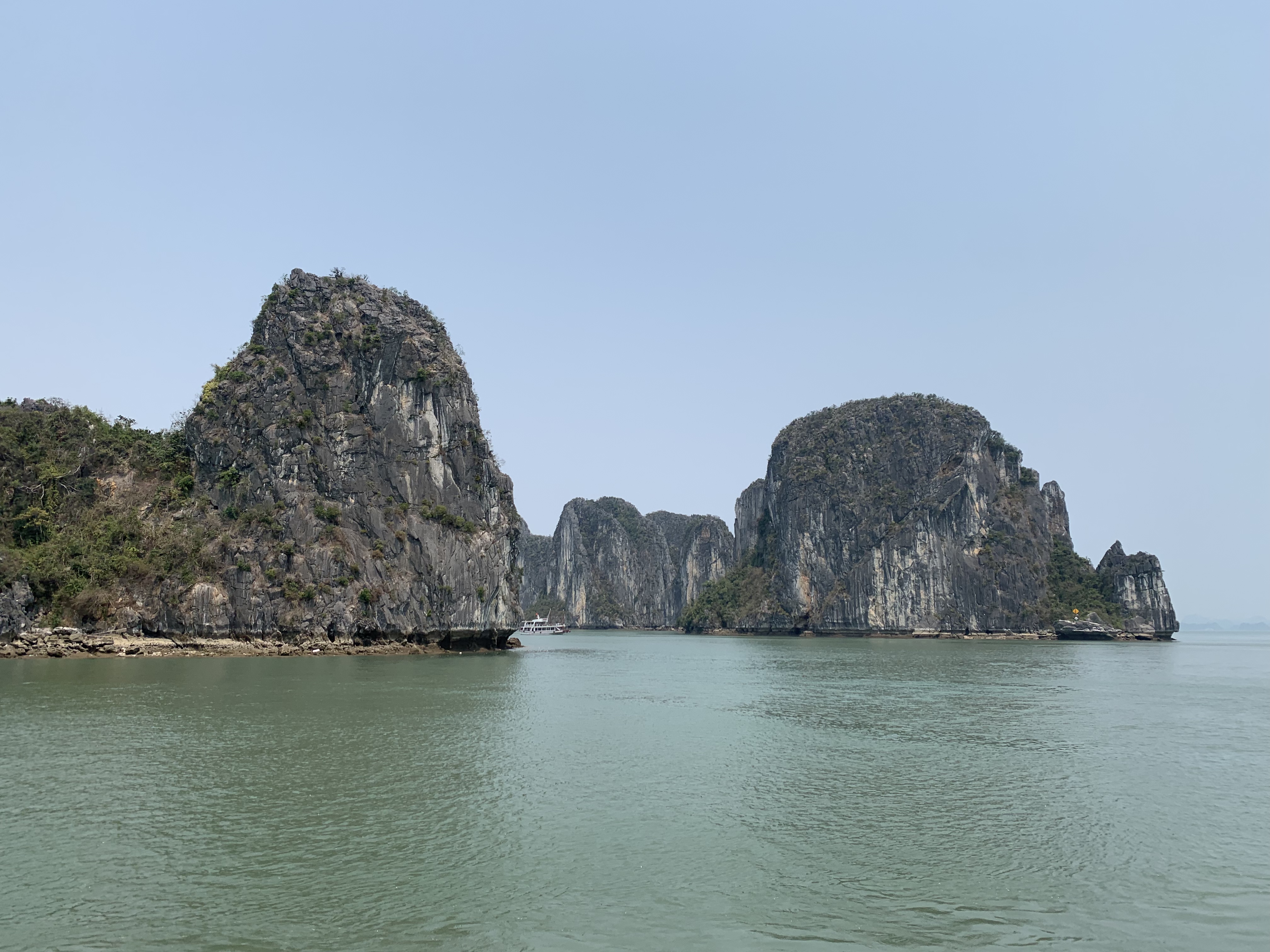 Enorme kalkstenen rotsen die oprijzen uit het kalme water van Ha Long Bay onder een bewolkte lucht.