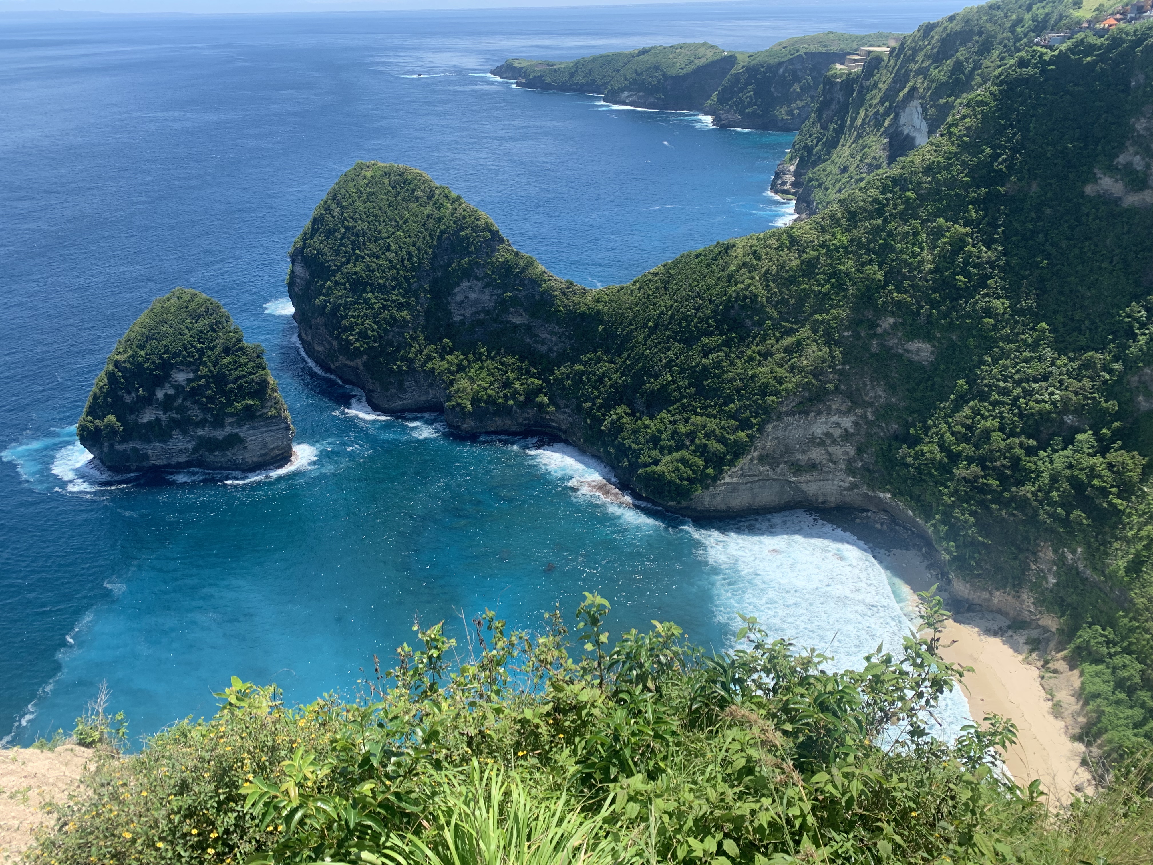 Uitzicht van bovenaf op de iconische rotskaap in de vorm van een T-Rex en het witte zandstrand aan de diepblauwe oceaan op Nusa Penida.