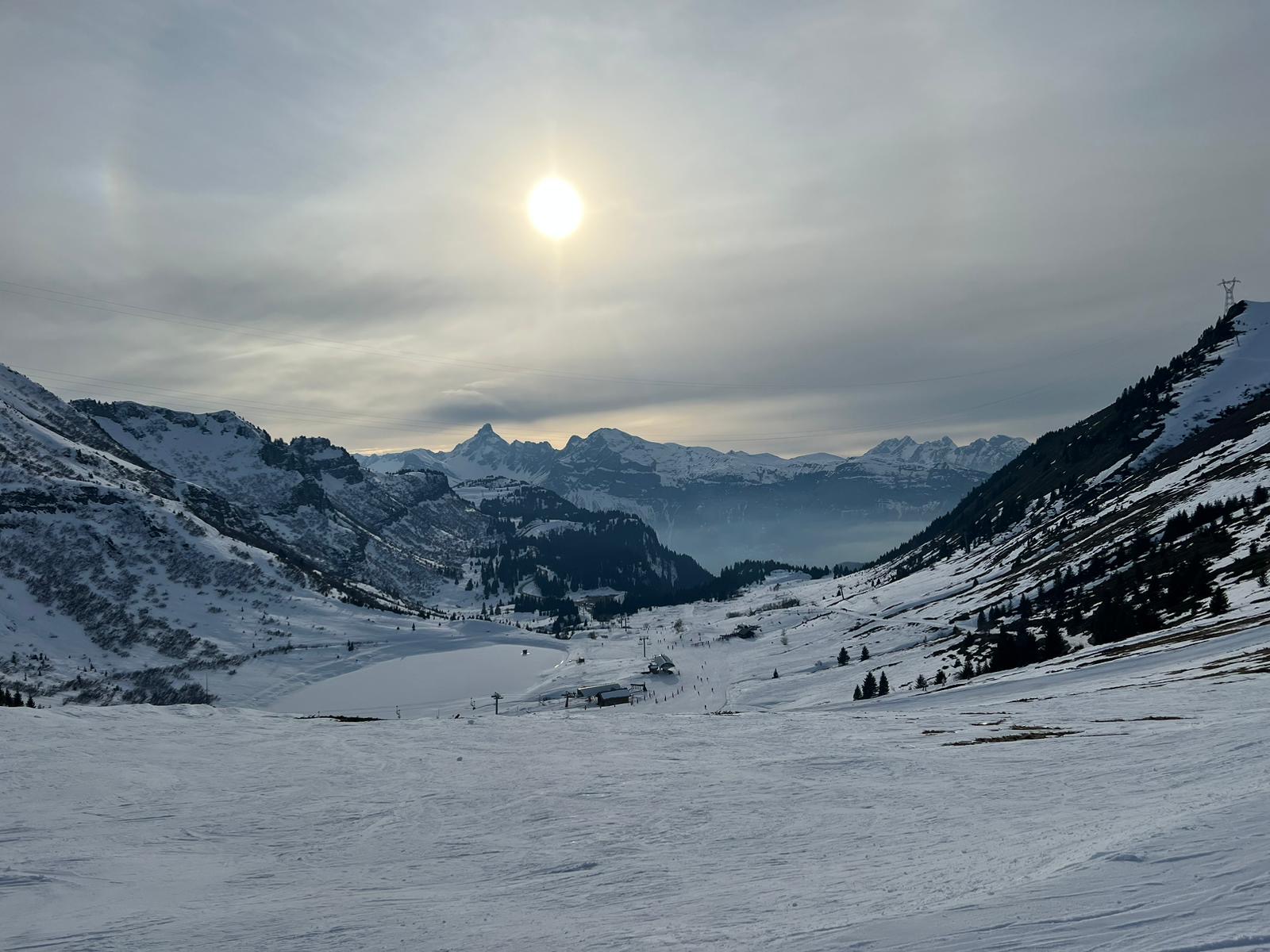 Besneeuwde alpentoppen en een bergmeer onder een felle winterzon aan een blauwe hemel.